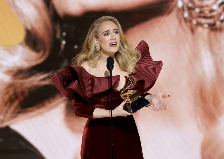 A woman in a gown speaks on stage, holding an award. 