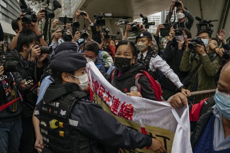 A woman surrounded by police officers raises a banner outside a court building.