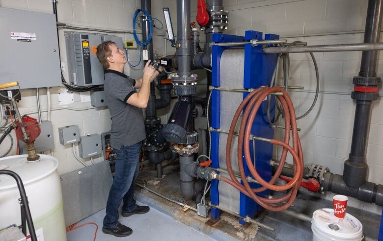 A man stands in front of pipes and equipment used to harness geothermal energy at an a community centre.