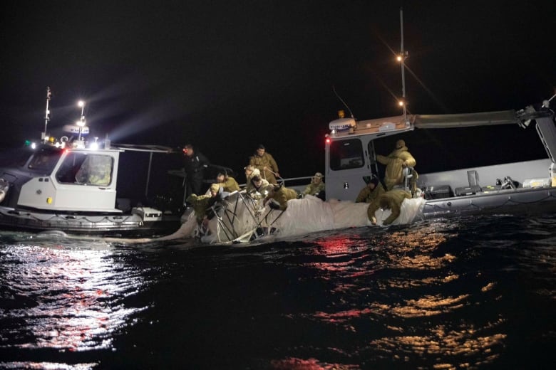 Night shot of boat recovering a large, white piece of material