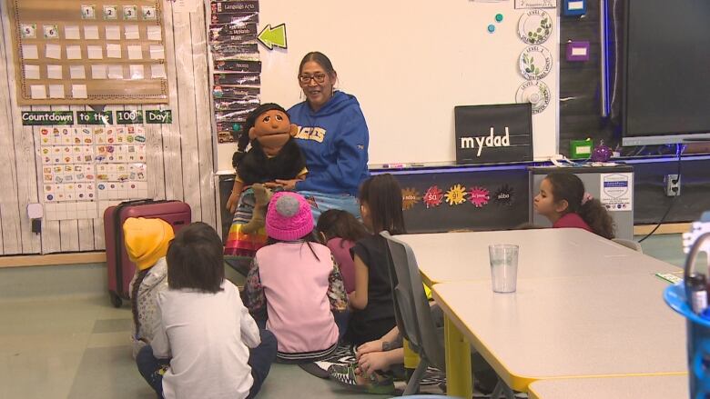 A woman sits in front of some children with a puppet.