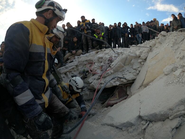 A line of people stand along a mound of concrete rubble.