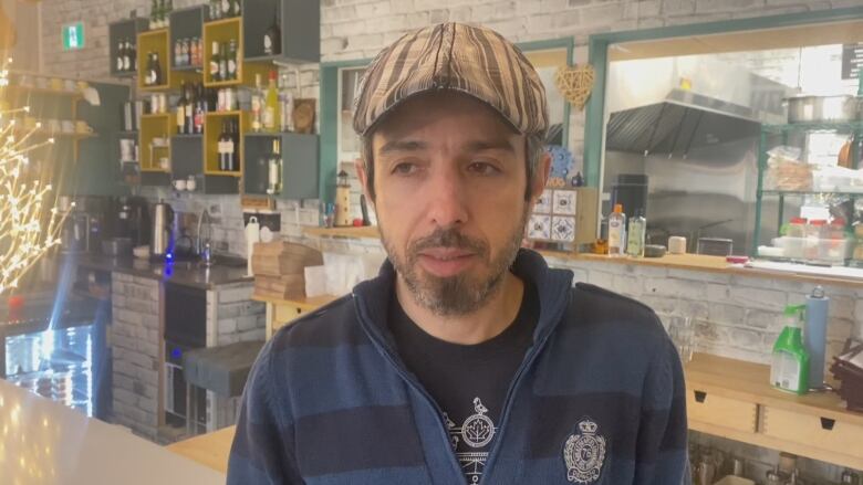 A man wearing a cap stands at a checkout counter at a grocery store. 