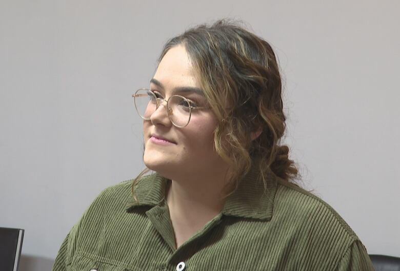 Woman with wavy brown hair tied back, wearing glasses and green corduroy shirt.