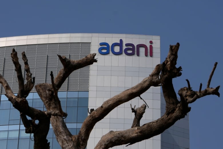 The bare branches of a tree are shown outside a grey and glass building, with the name 'Adani' on it.