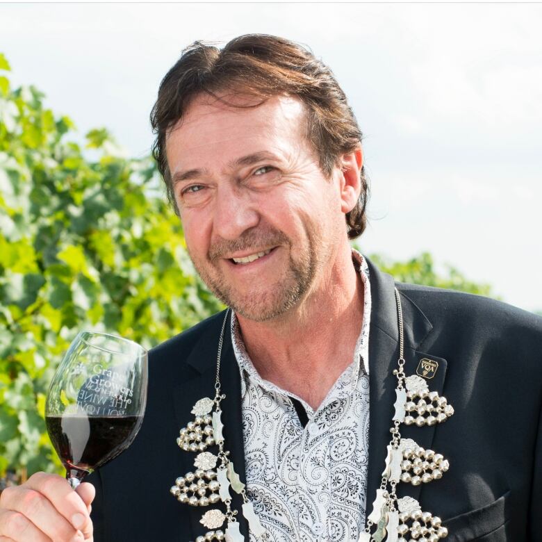 A man stands in a vineyard holding a glass of wine.