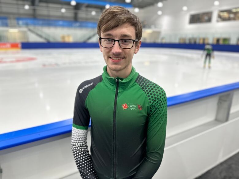 An athlete in a speed skating suit stands next to the ice. 