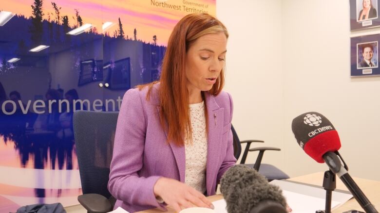 Red-haired woman in lilac suit at microphone.