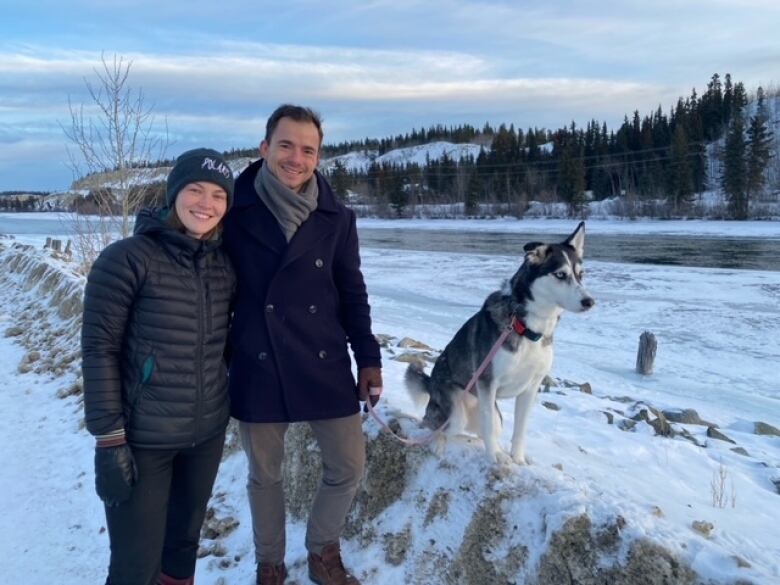 A proud couple smile and pose for a photo with their husky.