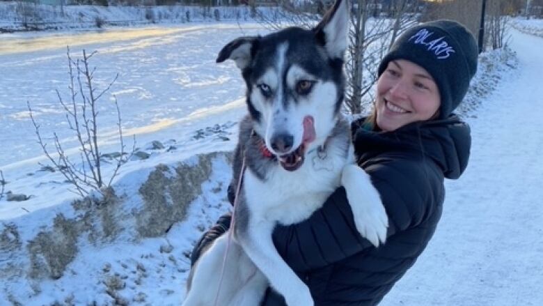 A grinning woman hefts a husky up in her arms.