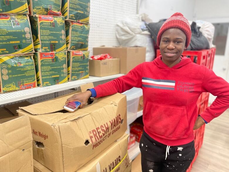 A Black woman in a red sweater stands next to cartons.