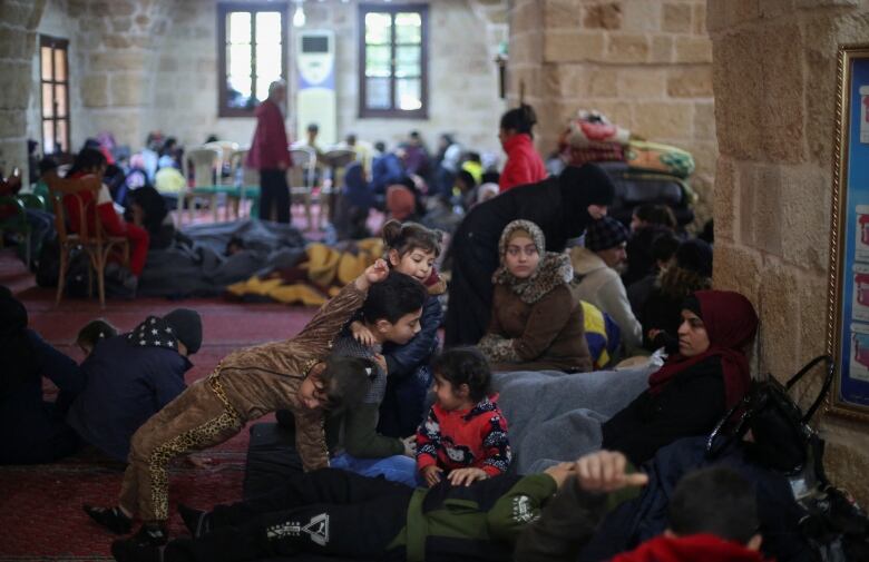 Women and children sit on the red carpet inside a brick building.