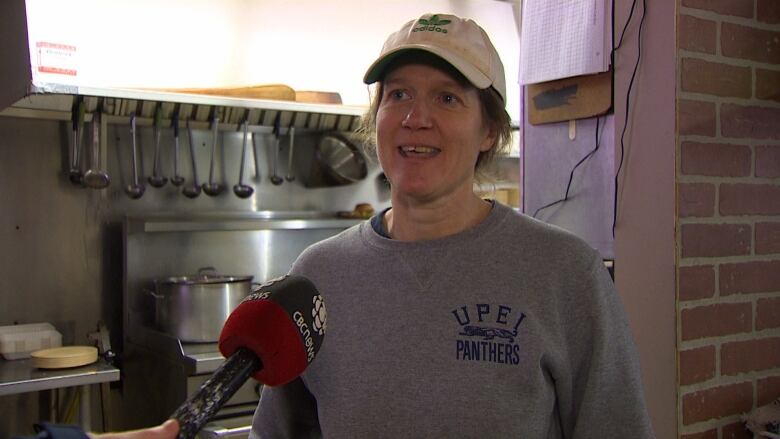 Woman wearing a baseball cap and grey sweatshirt.