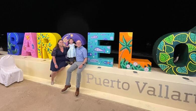 the family smiles in front of a sign that reads 'barcelo' 