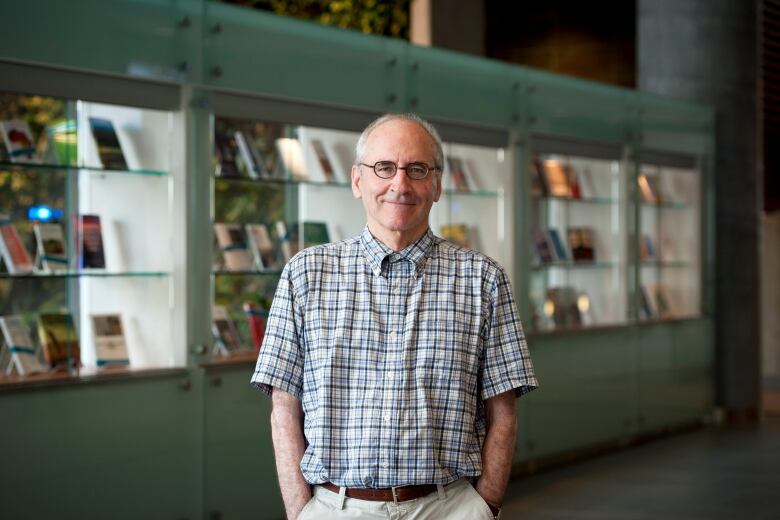 A man stands with his hands in his pockets in front of a display of books