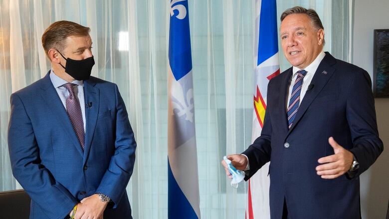 Two men talk to each other in front of the Newfoundland and Labrador and Quebec flags