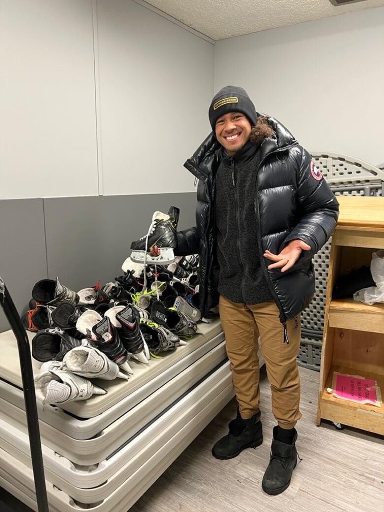 A man in a hat stands in front of a table covered in black and white figure skates.