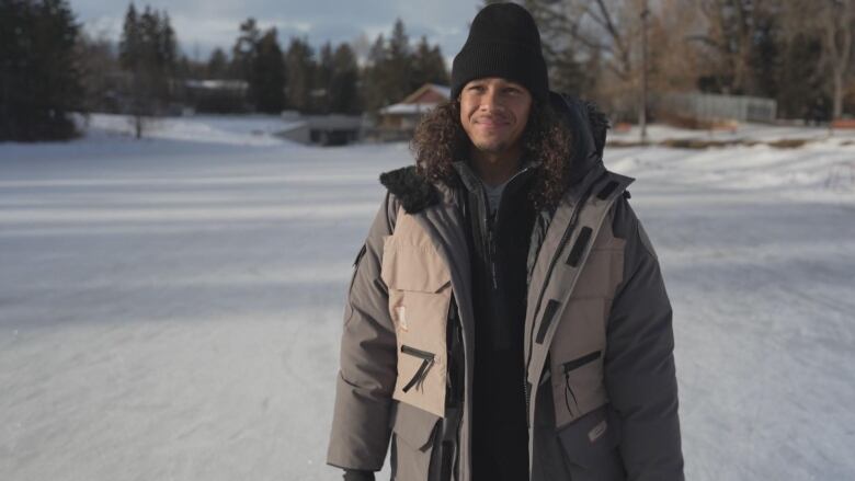 A man in a coat and hat stands on an ice rink.