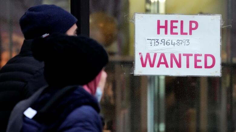 People look at a help wanted sign on a window.