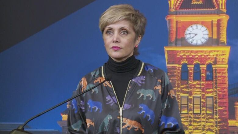 a woman with short hair stands near a microphone. she is wearing a blazer with tigers all over it 