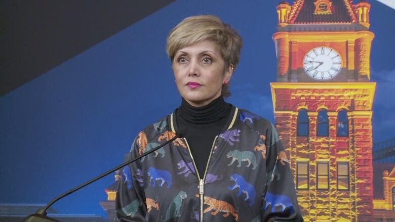 a woman with short hair stands near a microphone. she is wearing a blazer with tigers all over it 