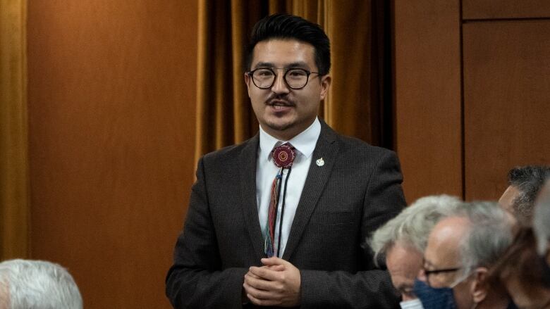 A man in a suit speaks in a crowd.