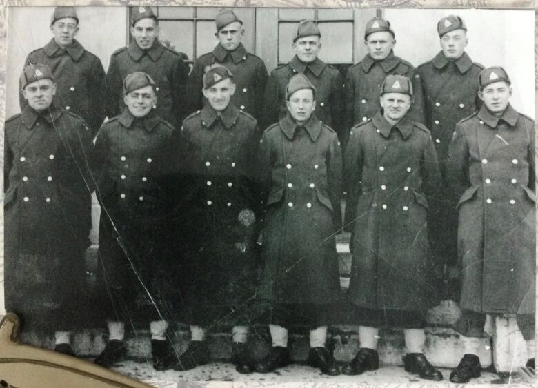 A group of young soldiers pictured in uniform, standing on a staircase outside, wearing heavy overcoats and winter hats. 