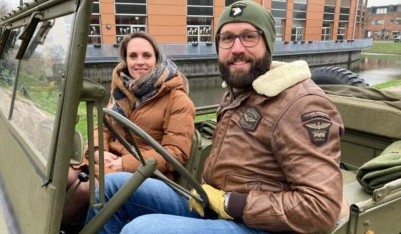 A young man and woman sit in a military jeep next to a canal.