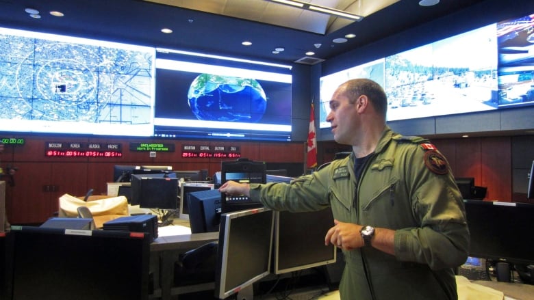 A person is seen in a command centre filled with TV and computer screens.