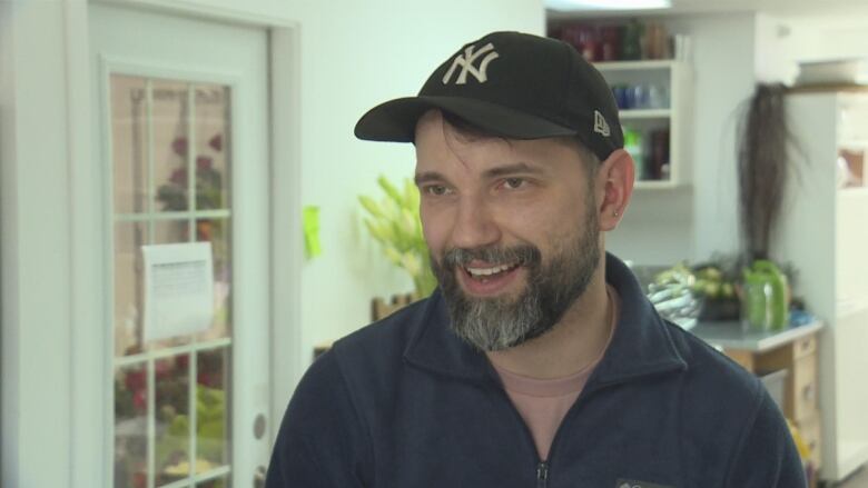 a man smiles - he is wearing a black ballcap and a zipped up sweater