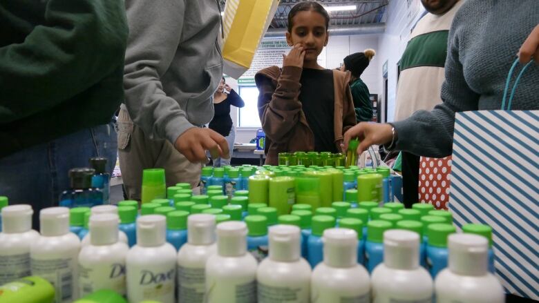 A young girl overlooks a table that is fully covered with lined up bottles of shampoos.