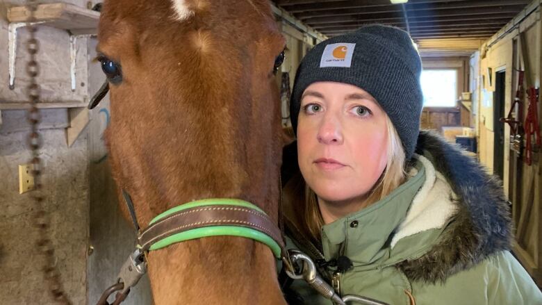 A woman with cropped blonde hair and a hat holds her face near that of a horse.