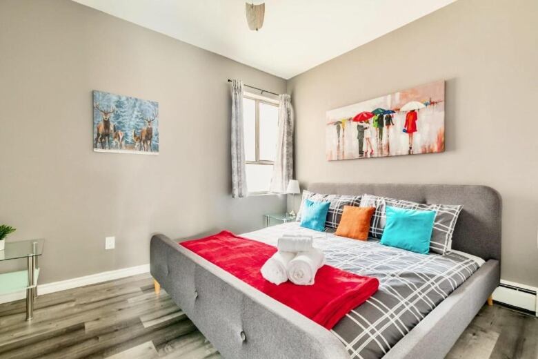 A bedroom with a neatly made bed and rolled up towels placed on top.