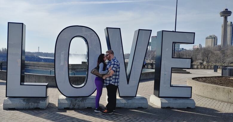 A man and a woman share a kiss in front of a sign reading 