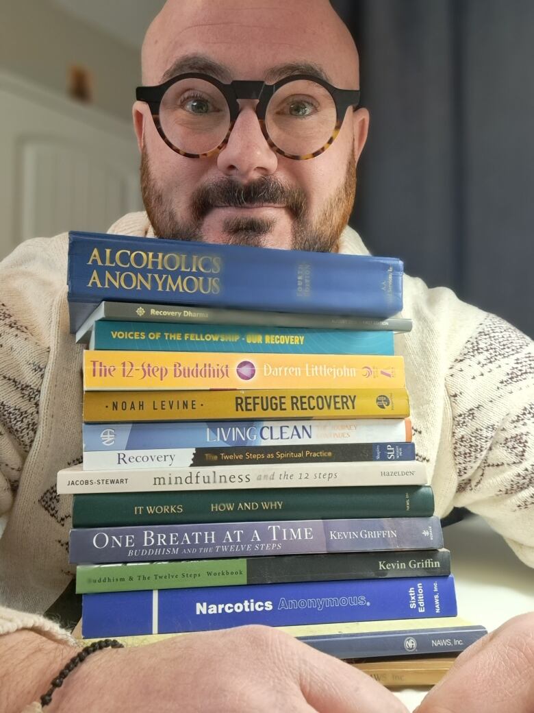 A man holds onto a large stack of books focused on treatment for drug and alcohol addiction.