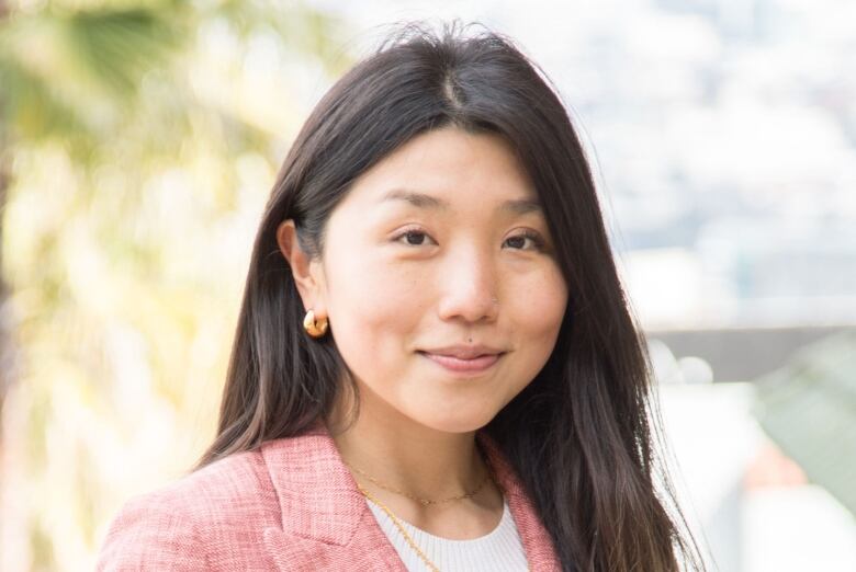 Woman, with a pink blazer, smiles posing for the camera.