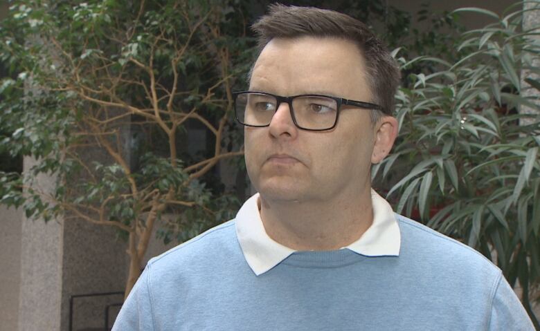 A man with glasses stands in front of plants.