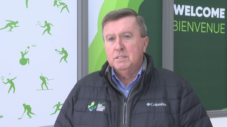 Man with grey hair wears black puffer jacket with 2023 Canada Games logo.