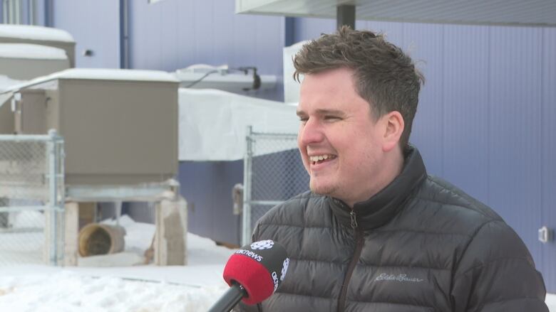 Man with short dark hair wearing black puffer jacket, smiling.