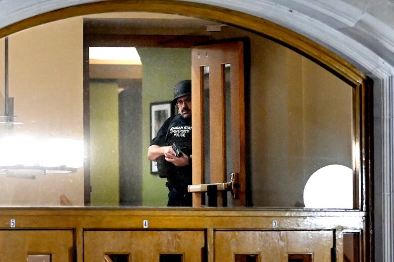 A police officer, with his gun drawn, is seen through the window at an entrance of a building on the Michigan State University campus.