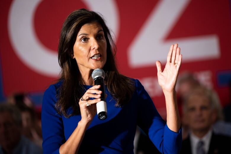 A woman is shown standing and speaking into a microphone.