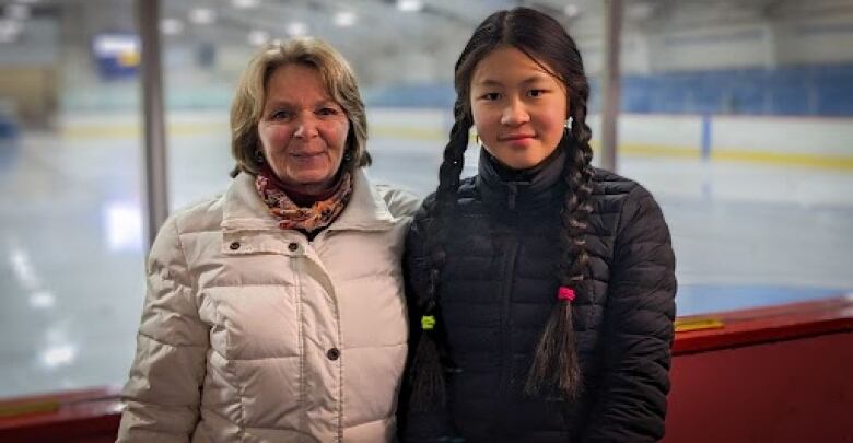 A coach and figure skater stand next to the glass at a rink 