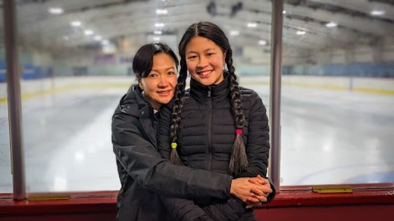 A mom hugs her daughter and they both smile, next to a rink 