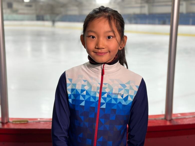 A young figure skater stands next to the ice. 