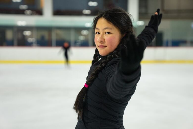 A young figure skater poses at the end of her program with her arm in the air. 