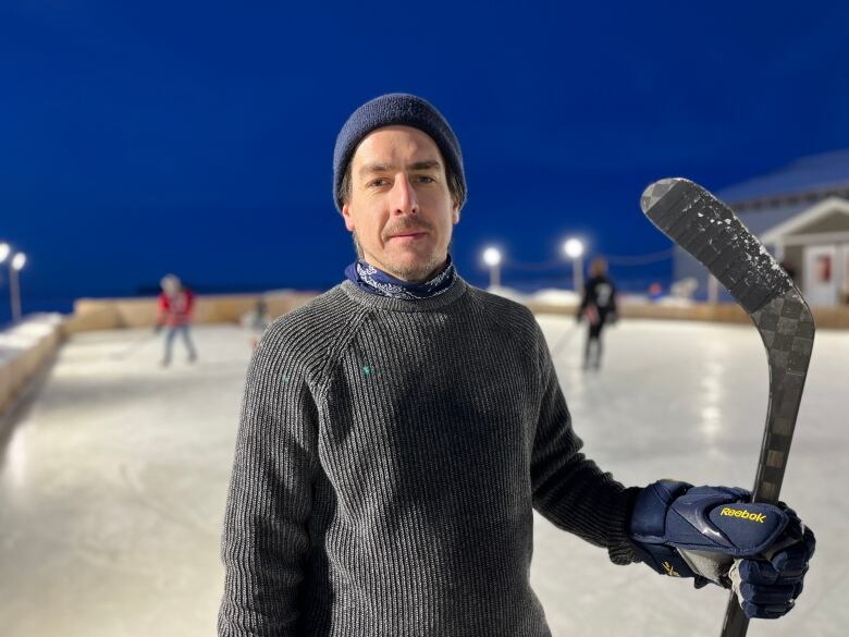 A man holds a hockey stick at an outdoor rink.