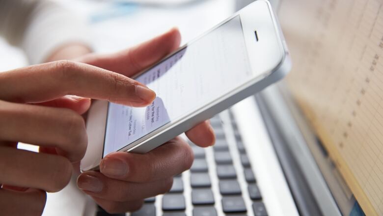 A hand holds a mobile phone with a laptop keyboard in the background.