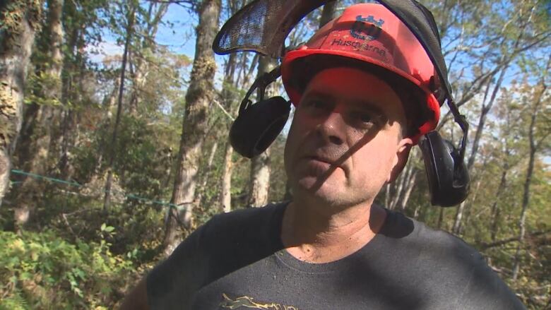 A man stands in the woods with a hard hat and ear protection.