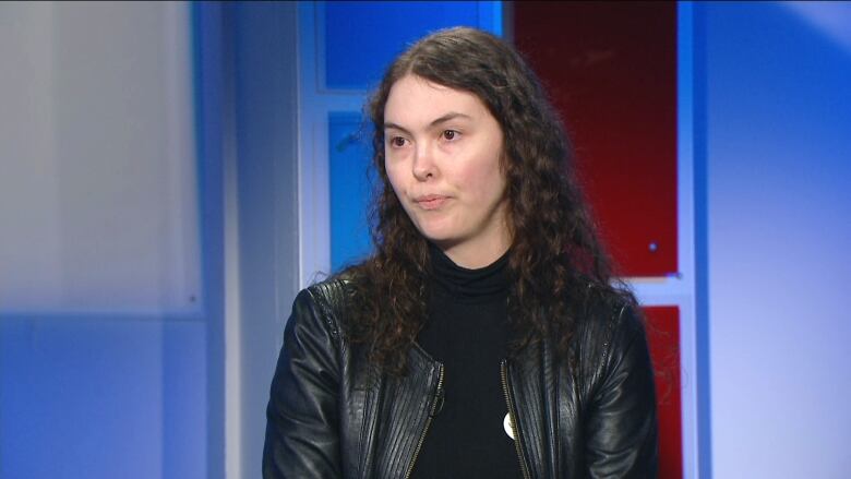 A woman in a black leather jacket sits in a TV studio.