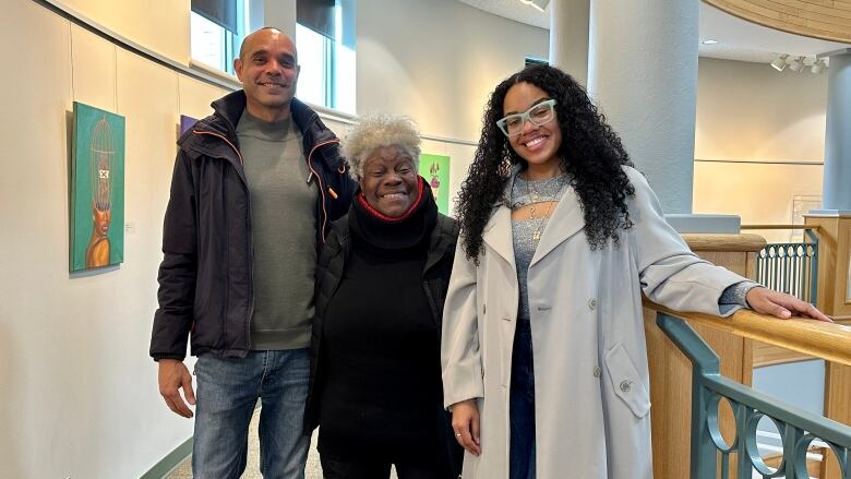 A smiling, elderly Black woman is flanked by two Black artists in the Richmond Cultural Centre.